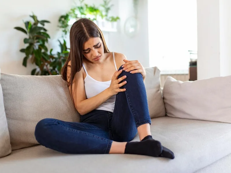 A woman sitting on a sofa holding her knee with both hands