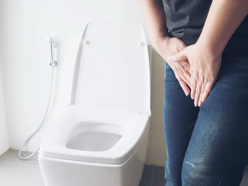 A person standing beside a toilet with their hands pressed between their thighs