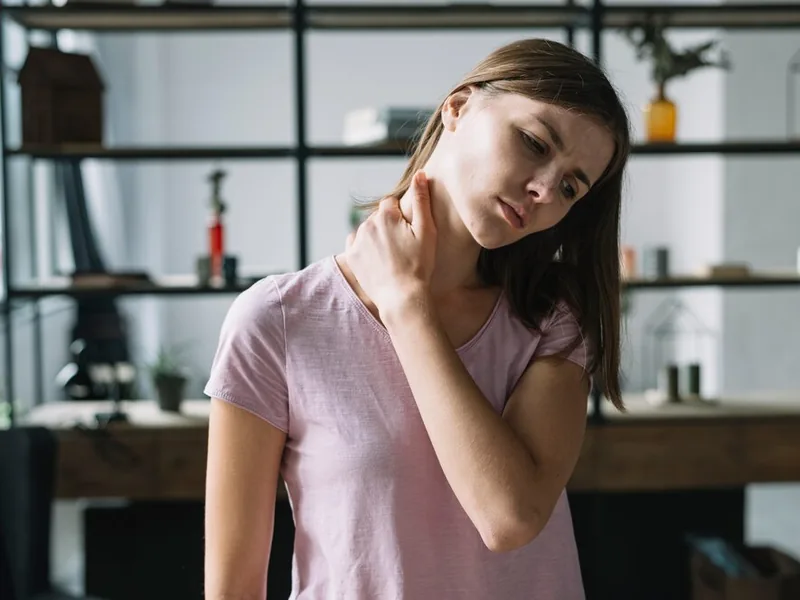 A woman tilting her head and holding the side of her neck