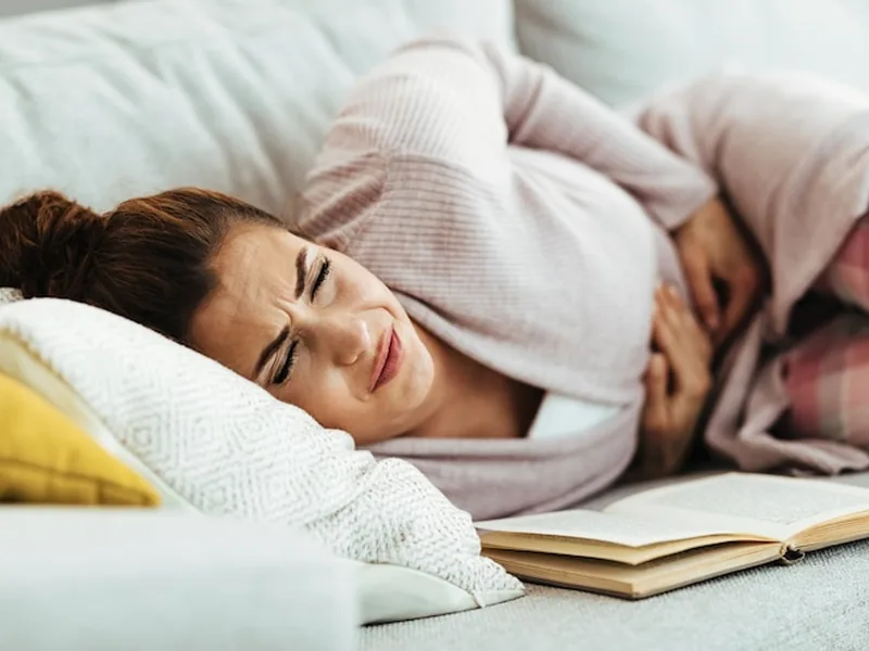 A woman lying in bed with her eyes closed, pressing into a pillow in discomfort