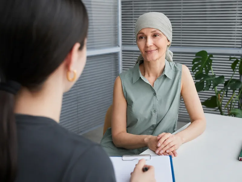 A patient wearing a head scarf talking with a clinician who is taking notes