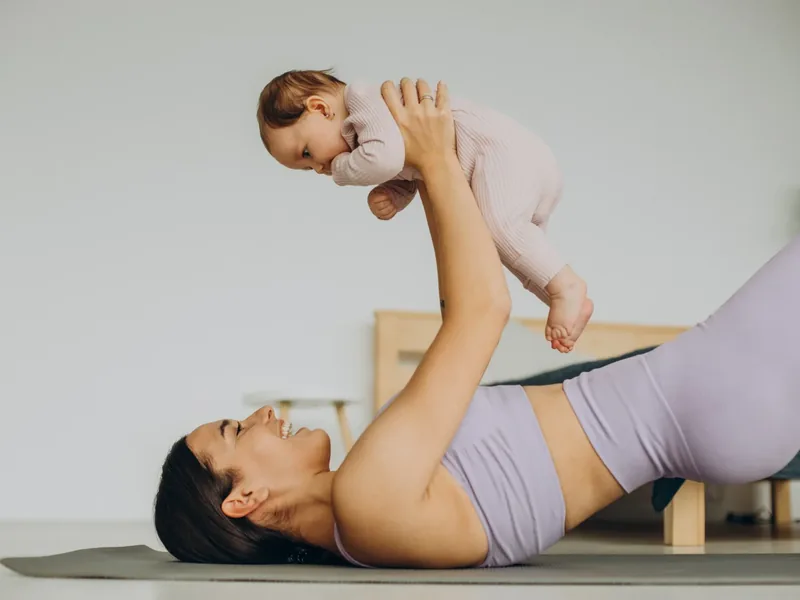A mother lying on an exercise mat lifting her baby overhead