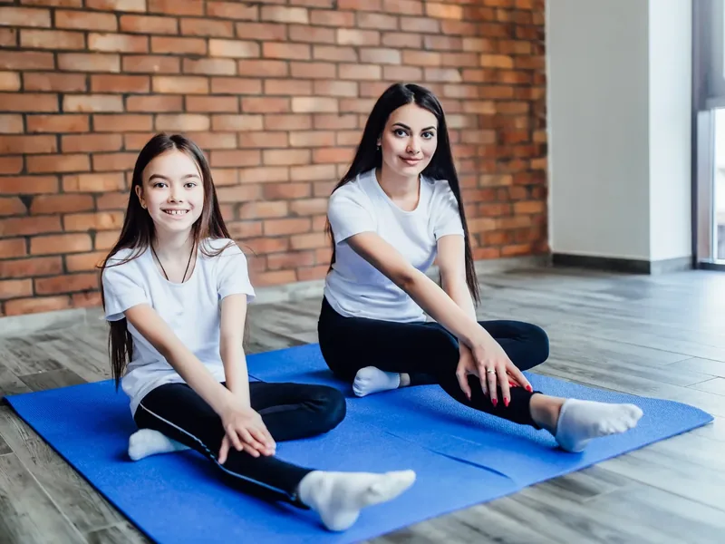 A teenager and a younger child stretching together on a mat