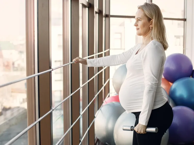 A pregnant woman doing a supported standing exercise at a studio barre