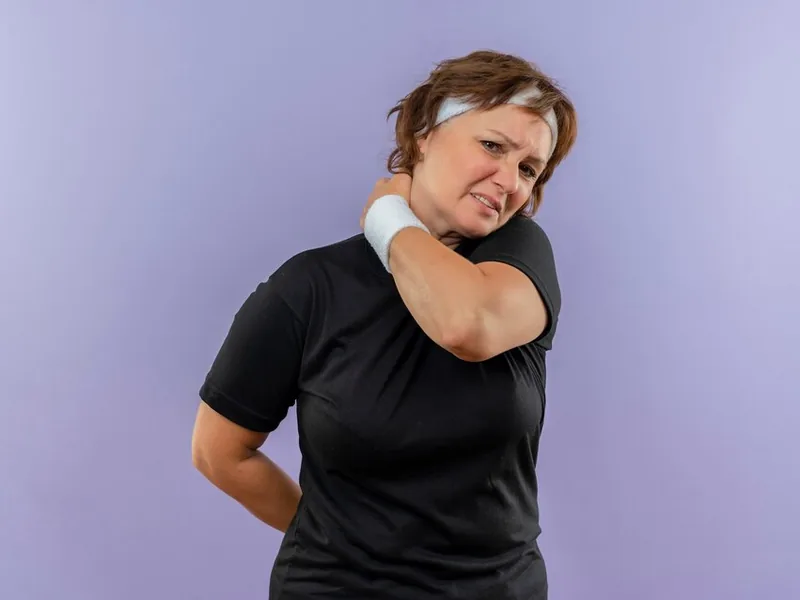 A woman reaching across to hold her opposite shoulder, wincing