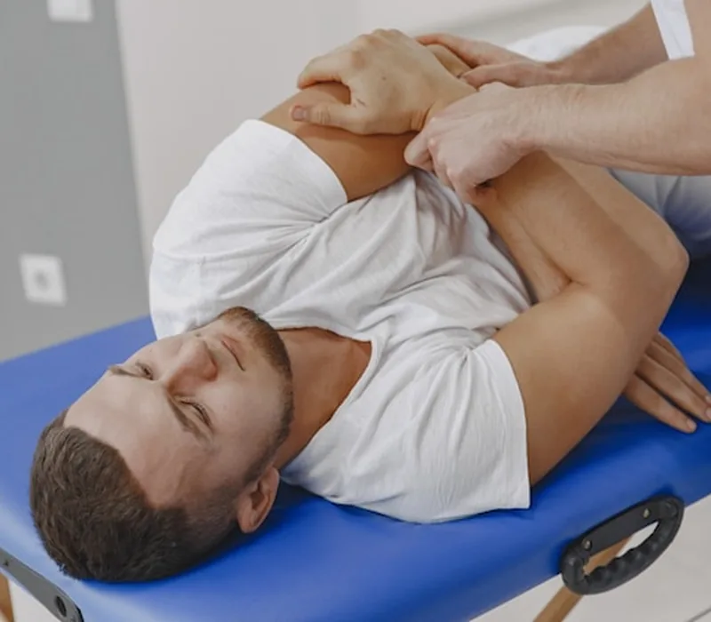 Therapist's hands working along the shoulder of a patient lying face up on a treatment table