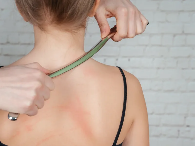 A curved IASTM tool drawn across the skin of a patient&rsquo;s upper back