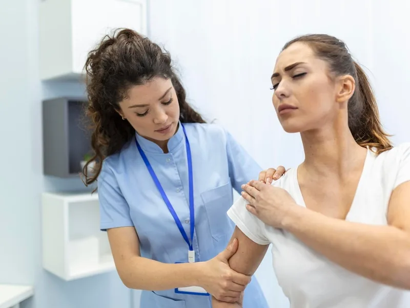A clinician in blue scrubs working along a patient&rsquo;s upper arm and shoulder